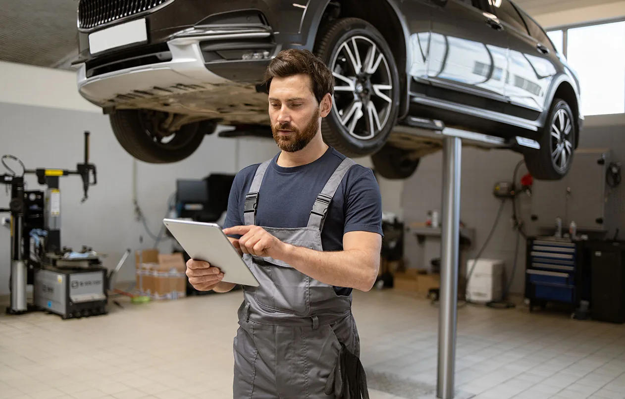 Mechaniker mit Tablet vor einem Fahrzeug auf der Hebebühne in der Werkstatt